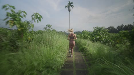 Detrás-De-Una-Joven-Mujer-Activa-Con-Ropa-Deportiva-Corriendo-Por-Un-Camino-Tropical-En-La-Naturaleza-De-Bali