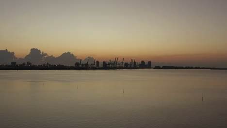 Aerial-view-silhouette-Miami-shipping-port-cranes-on-coastal-horizon-during-sunset