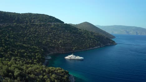 Aerial-view-over-Kefalonia-island-landscape,-luxury-yacht-anchored-on-emerald-water-coastline