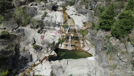 People-relaxing-on-rocks-next-to-natural-pool-at-Cascatas-de-Fecha-de-Barjas-in-Peneda-Geres-National-park,-Portugal