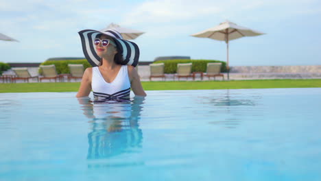 Zufriedene-Bemerkenswerte-Asiatin-Im-Pool-Des-Luxusresorts-Mit-Sommerhut-Und-Sonnenbrille,-Statischer-Kopienraum