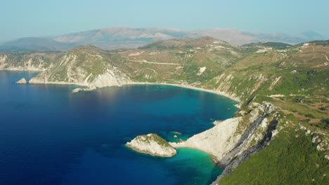Aerial-flying-towards-scenic-Petani-beach-surrounded-by-mountain-cliffs,-Kefalonia-Island