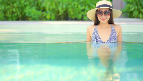 Beautiful-Stylish-Asian-Woman-in-Vivid-Pool-of-Luxury-Resort-Looking-and-Smiling-To-Camera,-Static-Shot-With-Copy-Space