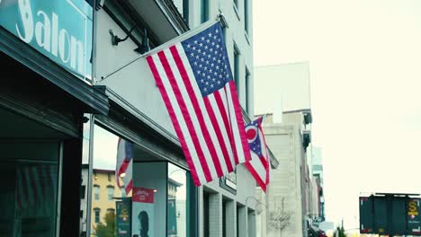 US-and-Ohio-American-flags-hang-in-the-bresze-in-front-of-a-small-business-over-the-sidewalk-in-a-small-quaint-town