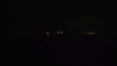 Öresundsbron-Bei-Nacht-Mit-Zwei-Blau-gelben-Säulen,-Die-Im-Dunkeln-Leuchten,-Und-Autos,-Die-Auf-Der-Brücke-Fahren