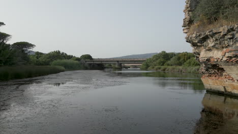 Drohne-Schoss-Tief-Nach-Vorne-Fliegend-An-Einer-Alten-Römischen-Ruine-Vorbei-Und-Flog-über-Das-Ruhige-Wasser-Eines-Flusses-In-Südspanien