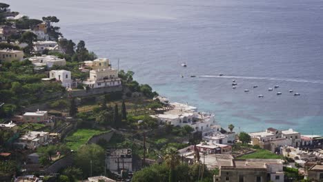 Aerial-view-of-Capri-village,-sea-and-boats-passing-during-a-sunny-day