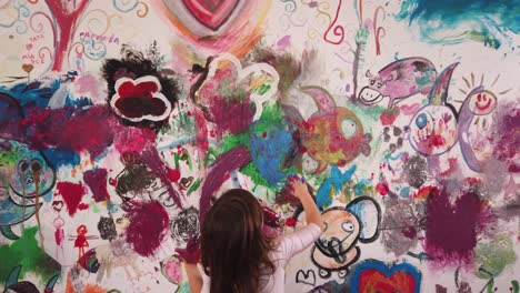 child-hand-painting-a-blue-heart-on-a-colorful-wall-and-wearing-a-pink-dancing-dress