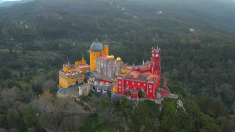 Aerial-pullback-Colorful-Pena-Palace-on-a-steep-hill-surrounded-by-Forest,-Sintra