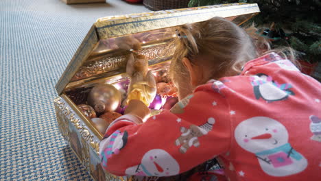 A-little-girl-opens-a-golden-box-to-find-Christmas-ornaments-to-decorate-the-Christmas-tree-with