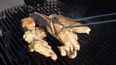 Organic-chicken-breasts-grilling-on-the-BBQ---turning-them-with-tongs-as-they-cook-in-slow-motion