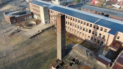 Aerial-orbiting-shot-around-brick-chimney-at-old-closed-factory-building,-site-of-former-silk-mill