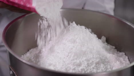 Icing-sugar-is-poured-in-to-a-large-metallic-mixing-bowl-in-close-up