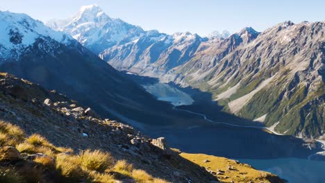 Panorama-shot-of-mountain-range-with-snowy-peak,-flowing-river-into-lake-during-sunny-day-on-Mount-Cook,New-Zealand