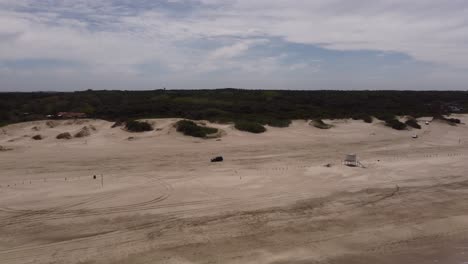 Aerial-tracking-shot-of-4x4-vehicle-driving-on-sandy-beach-of-Mar-de-las-Pampas-during-sunlight---Ocean-waves-reaching-shoreline
