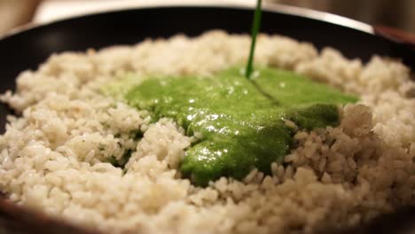 Pouring-green-spinach-puree-into-a-pan-full-of-cooked-rice,-SLOW-MOTION