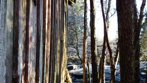 Tilt-down-shot-of-wooden-hut-side-facade-near-stream-in-forest