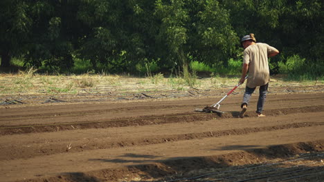 Unrecognizable-farmer-using-a-rake-for-plowing-the-field-and-making-furrows,-cultivating-concept