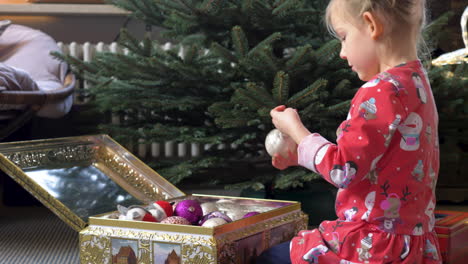 Junges-Kind-Trägt-Rote-Pyjamas,-Die-Ornamente-Auf-Einen-Weihnachtsbaum-Setzen