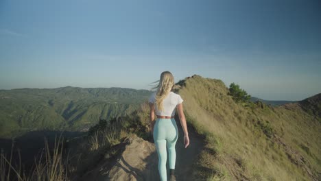 Fit-blond-woman-walking-on-edge-of-Mount-Batur-in-Bali-during-sunrise,-hiking-trip