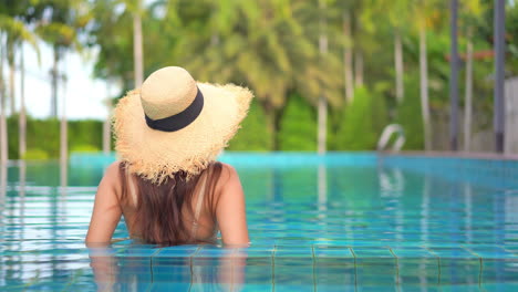 A-woman-wearing-a-straw-hat,-relaxing-in-an-infinity-pool-at-a-luxury-hotel