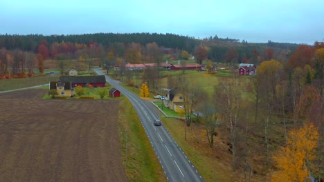 Aerial-view-car-driving-through-Beautiful-small-village,-Swedish-countryside,-Autumn-Colors