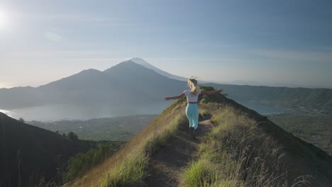 Young-female-athlete-running-on-mountain-ridge-in-Bali-spreading-arms,-concept-of-freedom