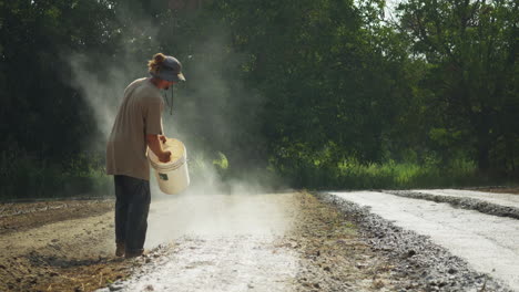 Agricultor-Esparciendo-Fertilizante-Orgánico-Blanco-En-Los-Surcos-De-Un-Campo-Agrícola,-Trabajador-Rural-Descalzo