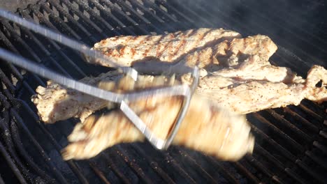 Turning-organic,-free-range-chicken-breasts-grilling-on-the-backyard-BBQ-with-tongs---isolated