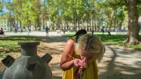 Close-up-of-young-woman-in-yellow-dress-drinking-from-public-water-fountain
