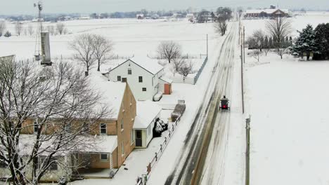 Aerial-follow-shot-of-Amish-horse-and-buggy-in-Lancaster-County-Pennsylvania-during-winter-snow