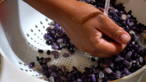 Hand-moving-black-beans-in-strainer-to-rinse-in-water,-Slowmo-Closeup