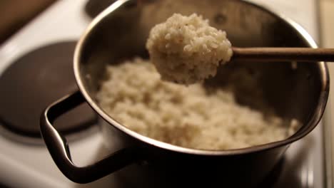 Shaking-cooked-white-rice-off-a-wooden-spoon-back-into-the-metallic-pot-on-the-stove,-SLOMO