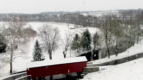 Aerial-reveal-of-red-covered-bridge-during-winter-snowstorm