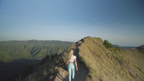 Blond-female-traveler-hiking-on-ridge-of-mount-Batur-at-dawn-in-Bali