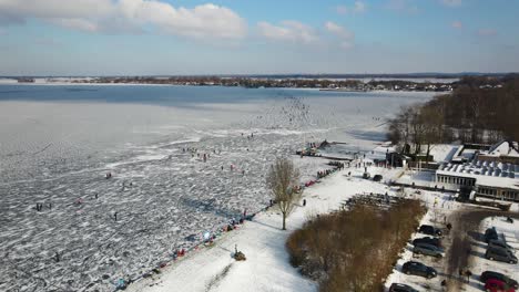 Aerial-flyover-parking-cars-beside-people-ice-skating-on-frozen-lake-in-winter---Netherlands,Europe