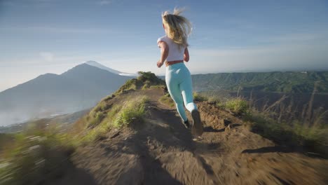 Fearless-blond-woman-running-fast-on-mountain-ridge-of-Batur,-high-on-life
