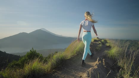 Mujer-Caminando-En-La-Cresta-Del-Monte-Batur-Con-Vista-De-Abang-Y-Agung-Durante-El-Amanecer