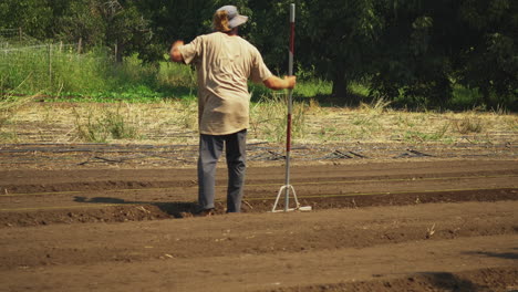 Farmer-leveling-the-field-with-a-hand-tool,-real-country-person-working-in-the-outdoor-during-a-sunny-day