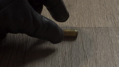 Gloved-criminal-hand-removing-fired-9mm-shell-casing-from-living-room-floor-and-removing-evidence-from-crime-scene