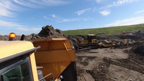 Action-cam-shot-of-a-dumper-truck-tipping-a-load-of-earth-in-front-of-a-bulldozer-and-roller