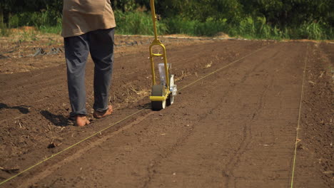 Barefoot-nature-lover-using-a-seeder-to-plant-organic-vegetables-in-a-local-farm,-still-shot