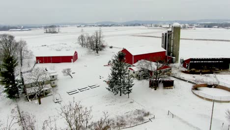Aerial-truck-shot-reveals-red-farm-buildings-against-white-snow