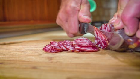 Close-up-shot-of-a-man-hands-cutting-thin-slices-of-salami-on-a-wooden-board