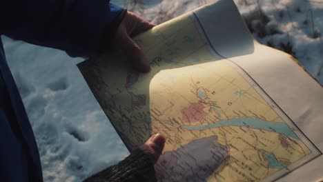 Adult-Holding-Map-On-Snow-Covered-Ground-With-Sun-Light-Hitting-Paper-Map