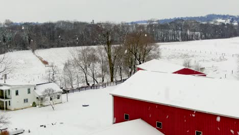 Reveal-shot-of-red-barn-and-farm-buildings,-silos-during-winter-snow