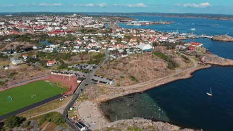 Beautiful-Scenery-Of-Houses-And-Streets-In-The-Port-Of-Pinnevik,-Lysekil,-Sweden-With-Boats-Smoothly-Sailing-Over-The-Sea-Water-On-A-Bright-Weather---Aerial-Shot