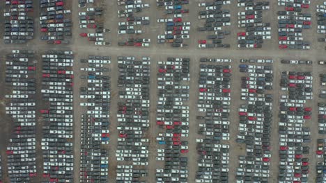Above-cenital-shot-of-brand-new-cars-parking-lot,-automobile-factory-top-down-drone-view,-zoom-in-of-a-group-of-vehicles