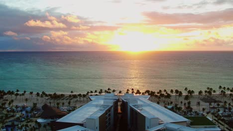 Tropical-sunset,-sunrise-above-luxury-vacation-and-holiday-resort-,-aerial-view-of-hotel-with-swimming-pool-and-beach-area-with-palms-and-blue-ocean