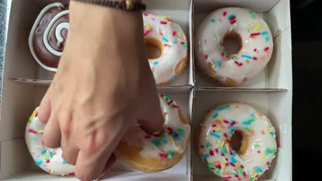 Weibliche-Hände-Pflücken-Donuts-Aus-Einer-Kiste-Auf-Schwarzem-Hintergrund